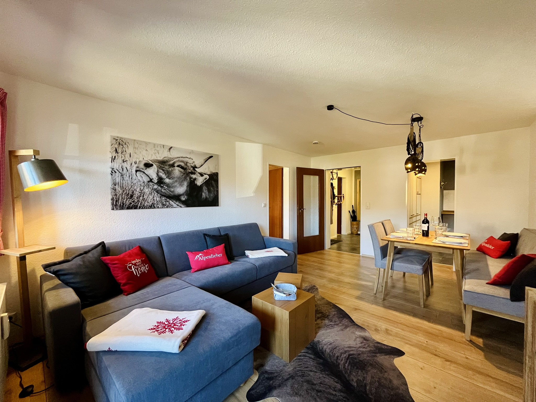Wohnbereich der Ferienwohnung Alpenfieber I mit grauem Ecksofa, roten Kissen und Essbereich