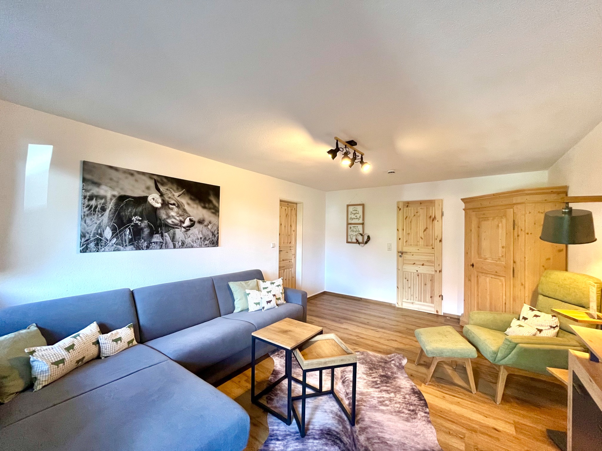 Wohnbereich der Ferienwohnung Alpenfieber II mit grauem Sofa, grünen Sesseln und Holzmöbeln